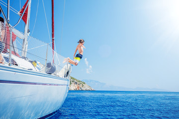 Boy jump in sea of sailing yacht on summer cruise. Travel adventure, yachting with child on...