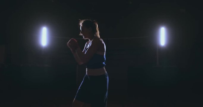 A beautiful sports boxer woman in red bandages on her hands and a blue t-shirt is fighting with a shadow practicing the speed and technique of punches. Camera movement side View. Steadicam shot