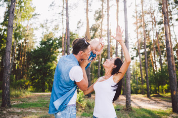 Family mom, dad and daughter sits at the daddy on the shoulders, and parents kiss on the nature in the forest in the summer at sunset