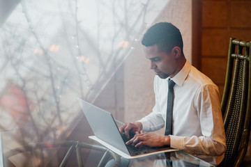 black man writing and working on laptop, notebook, in a white shirt, indoor, close-up