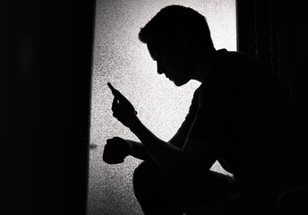 silhouette of young man reading on smartphone