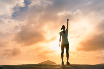 Feeling motivate- winning- strong. Young woman standing on mountain top with fist in air. 