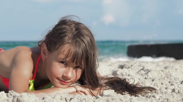 Child lying on sand and looking at camera. A cute little girl lies on the sand against the background of the sea.
