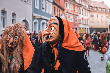 Funny witch with orange headscarf and black robe looks to the side. Street Carnival in Southern Germany - Black Forest.