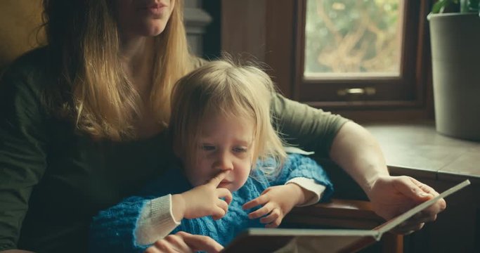 Young mother reading to her toddler by the window