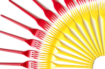 Plastic forks, red and yellow on a white background. Selective focus, top view.