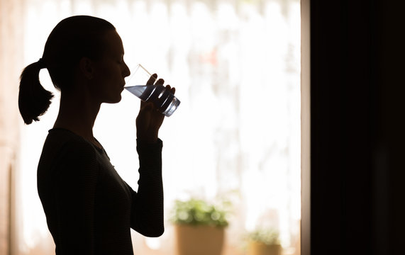 Silhouette Of Young Woman Drinking Glass Of Water At Home.