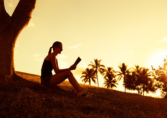 silhouette of young woman reading book on background of sunset