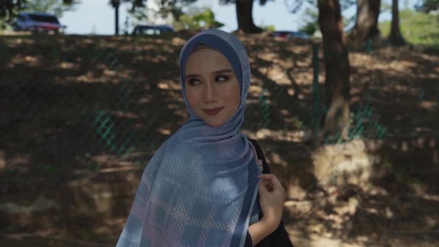 Muslim woman with hijab or scarf smiling and walking at park in slow motion. Young attractive Asian woman fashion.