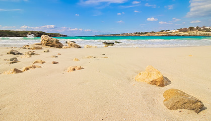 Salento beach, Taranto, Puglia, Italy, waves breaking on the coast and isolated stones on the sand, partly cloudy blue sky