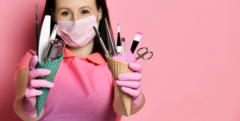 Closeup. Waffle cones with instruments for nails salon is kept at arms length by master in pink apron and medicine gloves and mask - Powered by Adobe