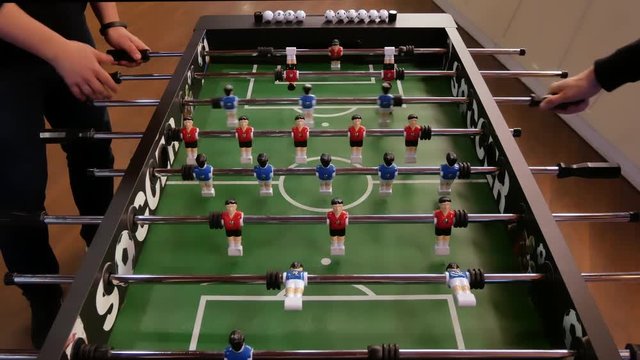 Friends having fun together playing foosball. Colleagues playing table football on break. People enjoying table soccer game. Close up of table football kicker game