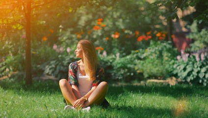 Happy young woman sitting outdoors in yoga position and meditating with closed eyes in summer park Peaceful girl enjoy rest smile and relax in tranquility in spring bloom. Mindset inner peace concept