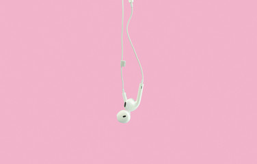 White hanging ear buds headphones isolated on a pink background