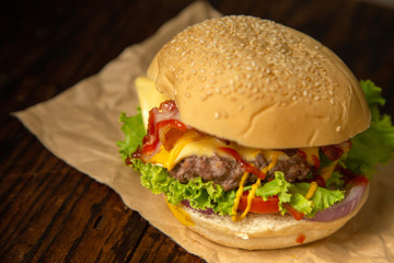 Cheesburger with grilled beef and bacon on paper in rustic style.