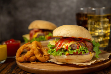 Cheesburger with grilled beef and bacon, onion rings and soft drinks in rustic style.