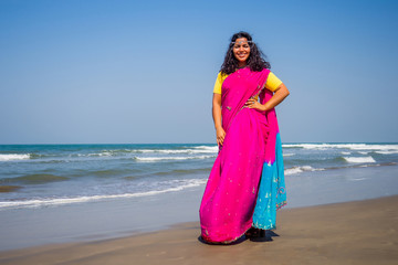 Fototapeta na wymiar portrait of a beautiful smiling snow-white smile indian woman black curly hair and dark skin in a pink sari holding bottle of sunscreen spray on beach.girl enjoying spf body paradise vacation