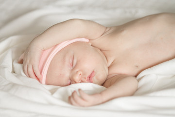 Close up of a sleeping naked newborn baby girl on a white blanket