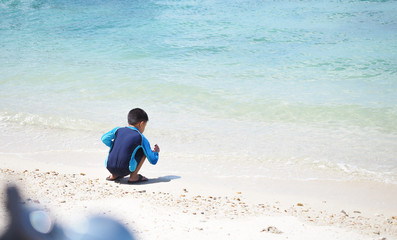Little boy is picking piece of shell from the white sand beach with curiosity.