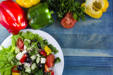 Vegetable salad cucumbers peppers cheese olives on a white plate on blue background copy space	