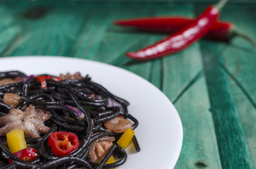 Fototapeta na wymiar Spicy black spaghetti dish with seafood and vegetables on a white plate green wooden background top view