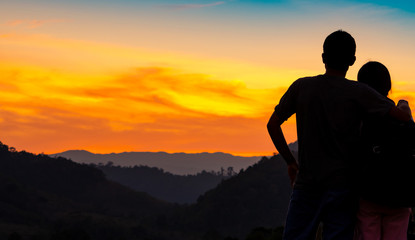 Back view of romantic couple watching beautiful sunset over mountain layer. Couple travel. Backpacker happy in love and travelling honeymoon. Silhouette of two tourist hiking to top of mountain.