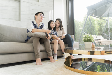happy asian family watching tv together on sofa in living room. family and home concept