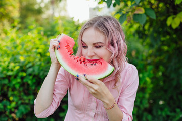 Beautiful young woman with pink hair enjoying watermelon