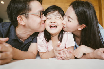 Obraz na płótnie Canvas Asian Parents kissing their little daughter on both cheeks. family portrait.
