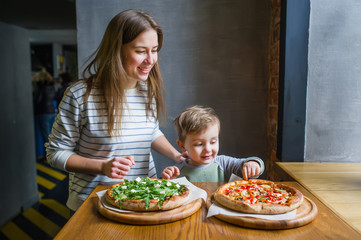 Young mother and cute little son eat pizza in restaurant.