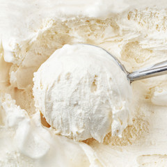 Vanilla ice cream with a scoop in  container as background. Macro. Scooped out ice-cream,  top view.