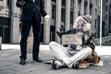 Grey-haired senior homeless carrying nameplate and taking bite food