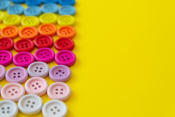 Multi-colored buttons on a yellow background. Button rainbow for clothes. Copy space