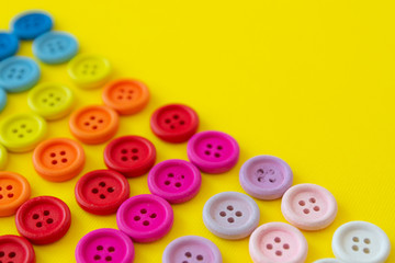 Multi-colored buttons on a yellow background. Button rainbow for clothes. Copy space