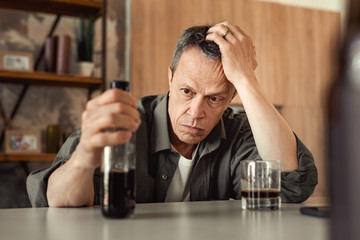 Apathetic short-haired man leaning on his hand and carrying partly-empty bottle