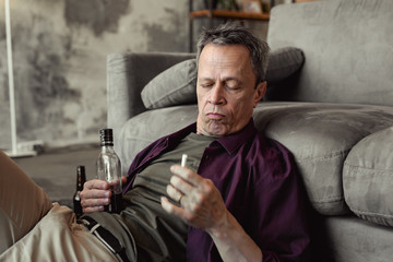 Drunk short-haired old man spending time at home with alcohol and smoking