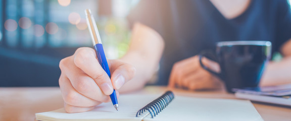 Business woman hand is writing on a notepad with a pen.