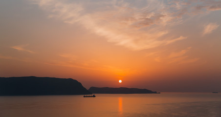 Naklejka na ściany i meble Cargo ship sailing away against orange sunset 