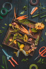 Florist workplace with orange and yellow flowers in a wooden box, tools, scissors, and floral tape. Wedding bouquet flowers flat lay