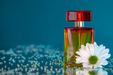 Macro photography of a yellow-red bottle of perfume standing on a mirror near a white flower among...