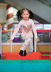 Happy Little Asian child girl play jumping at indoors playground.