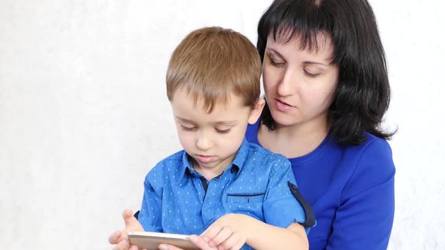 Woman and child look at the screen of the smartphone and laugh. Mom plays with her son in a developing game. Life in the network, applications and the Internet.