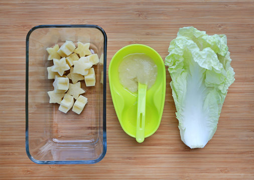 Frozen baby food homemade, yellow star from lettuce Cubes in square glass bowl on wooden board.