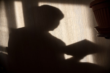 silhouette of young boy with book on wall by the window
