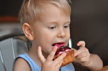 little blonde boy eats cake in the kitchen of the house