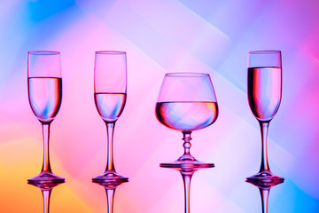 Four wine glasses of water are on the table, behind a colorful background.Glasses reflected in the glass.
