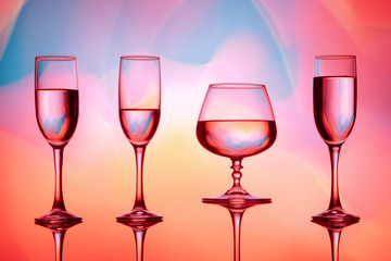 Four wine glasses of water are on the table, behind a colorful background.Glasses reflected in the glass.