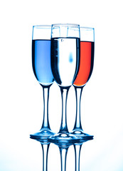 Three glasses of champagne, with liquid of different colors, on a blue background.