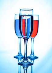 Three glasses of champagne, with liquid of different colors, on a blue background.