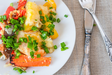 Vegetables baked with cheese in a white plate on a rustic background, top view, close-up, vegetable casserole - vegan dish